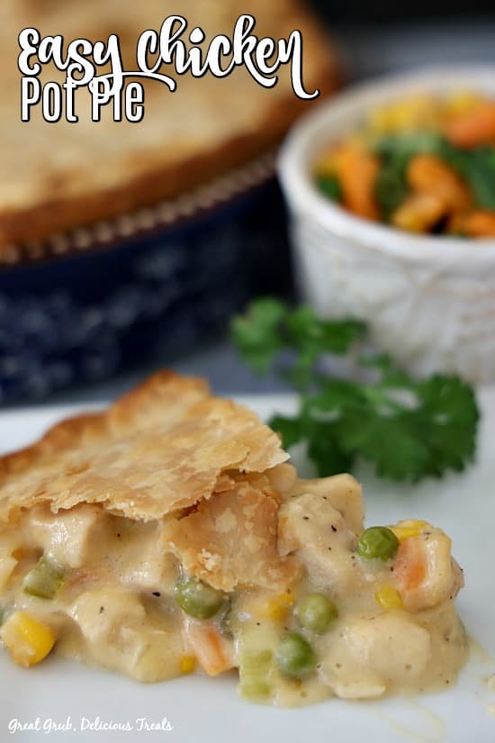 A slice of chicken pot pie on a white plate with a small white bowl filled with mixed veggies in the background next to a blue pie pan filled with chicken pot pie.