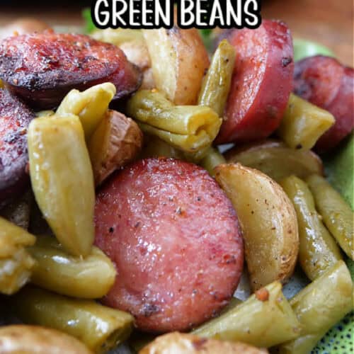 A green plate with sliced smoked sausage, potatoes, and green beans with the title of the recipe in text at the top.
