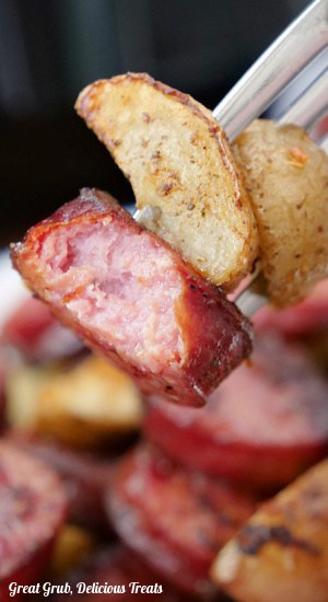 A close up of a bite of sausage and two small wedges of potatoes.