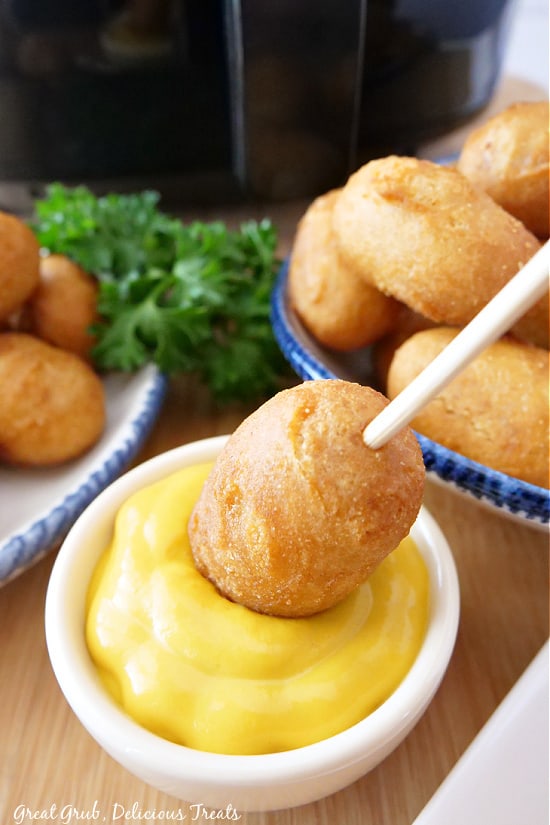 Mini Corn Dogs in Air Fryer are a quick and easy appetizer or meal to whip up in a matter of minutes. A mini corn dog on a stick being dipped in a small bowl of mustard.