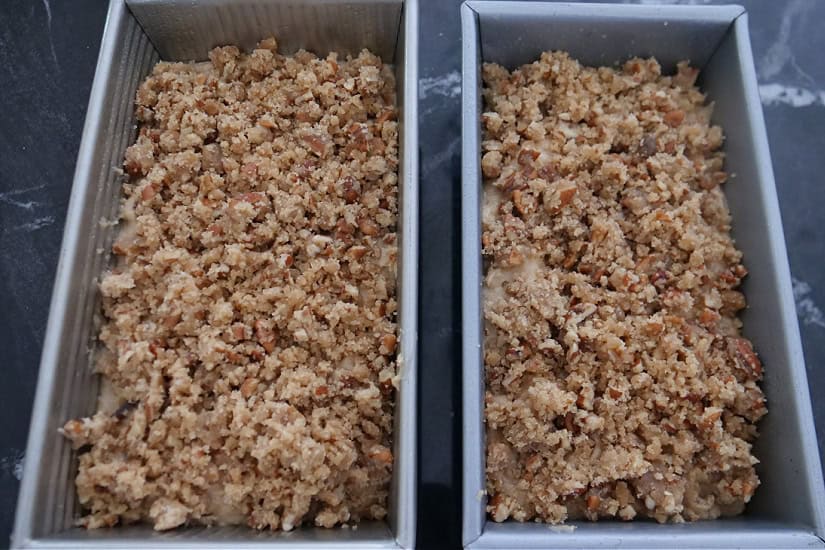 Two loaf pans with crunchy pecan topping added to the top of apple bread batter