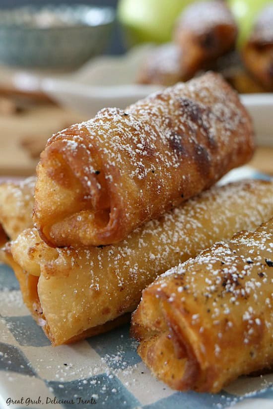 Apple Cream Cheese Egg Rolls are crispy, delicious and tastes like apple pie with a cream cheese filling. Four apple cream cheese eggs rolls sitting on a blue and white checkered plate.