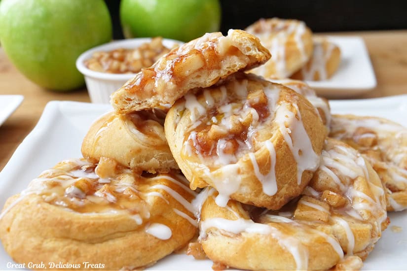 A horizontal photo of a half dozen apple pinwheels on a white plate with a bite taken out of the one on top.