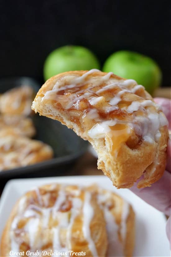 A close up of a apple pinwheel with a couple bites taken out of it and it is held up above the other pinwheels.