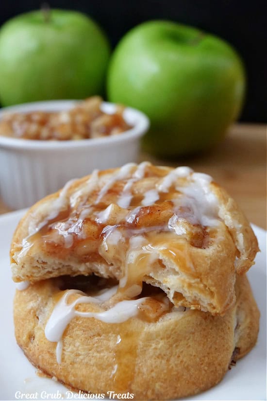 A white plate with two apple pinwheels on it with a bite taken out of the top one.