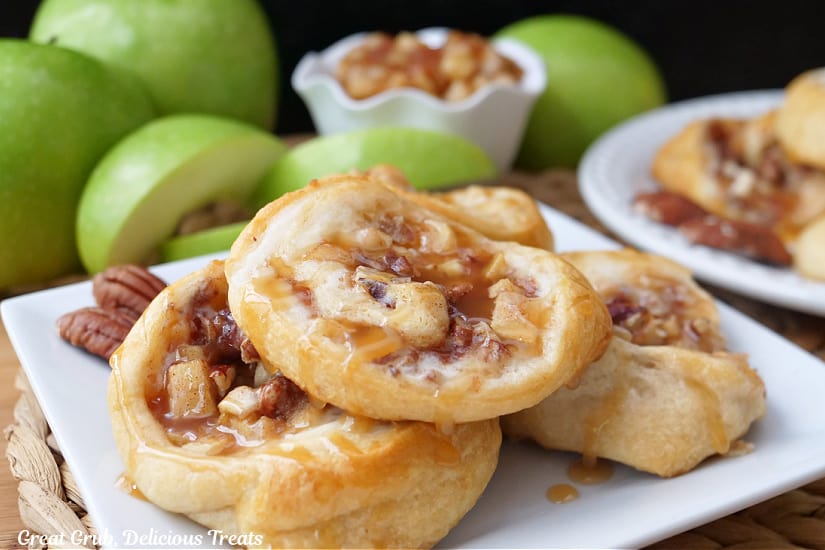 A white square plate with four apple crescents on it with green apples in the background.