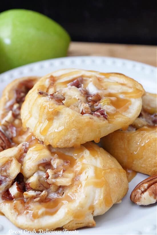 Four apple pecan crescent rolls on a white plate with a green apple in the background.