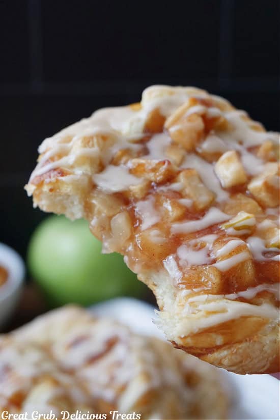 An apple pastry held cluse to the camera lens showing all the delicious details and the bite taken out of it.