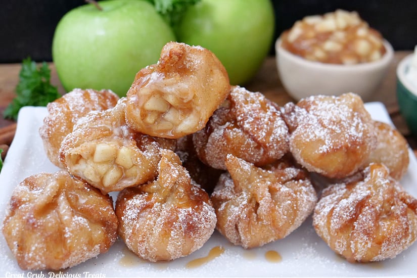 A horizontal photo of a white rectangle plate with 10 fried wontons filled with apple filling and drizzled with caramel sauce on it.