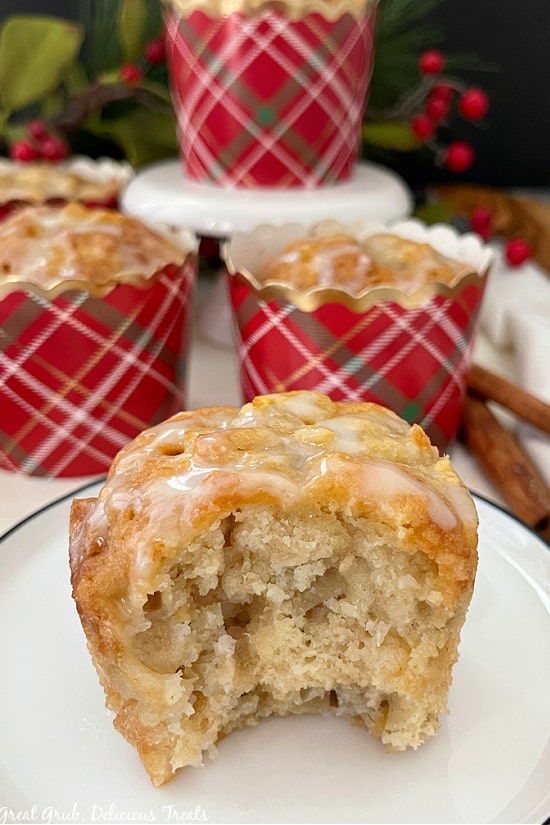Apple Muffins with Glaze are moist muffins loaded with diced apples and topped with a sweet vanilla glaze. A muffin on a small white plate with a bite taken out of it.