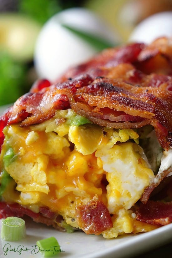 Bacon Breakfast Roll Ups Bacon, egg, cheese, avocado, green onions, sour cream breakfast wrap on a white plate.