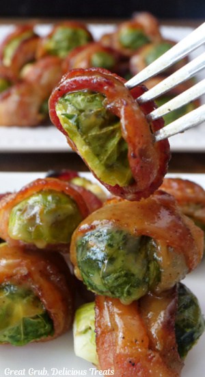 A plate filled with brussel sprouts that are wrapped in bacon with one of them on a fork.