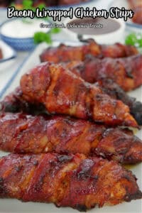 A white oblong plate with blue trim filled with half a dozen bacon wrapped smoked chicken strips.