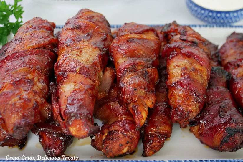 A white plate with blue trim with nine smoked bacon wrapped chicken tenderloins on it.