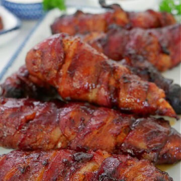 A white rectangle plate with blue trim with six smoked bacon wrapped chicken strips on it and the title of the recipe at the top.