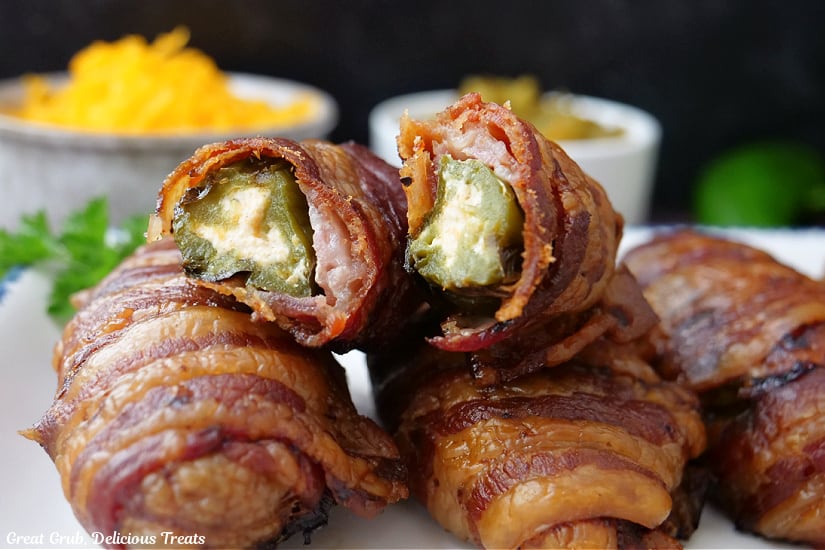 A horizontal photo of a white plate with five jalapeno poppers on it with one of the poppers cut in half.