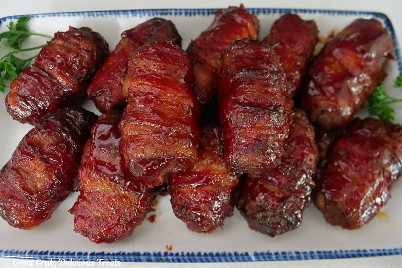 A white oblong plate with blue trim filled with a dozen smoked mini bacon wrapped meatloaves.