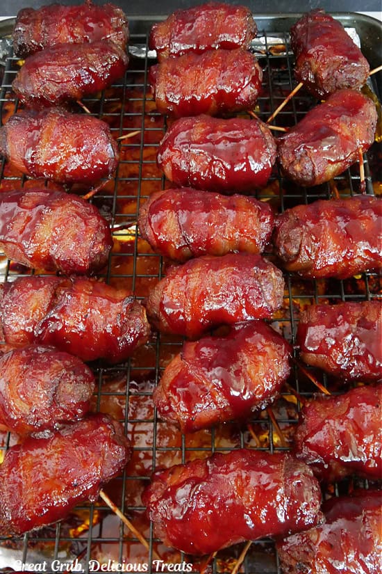 A baking sheet covered with foil with a rack on top with eighteen smoked mini bacon wrapped meatloaves on it.