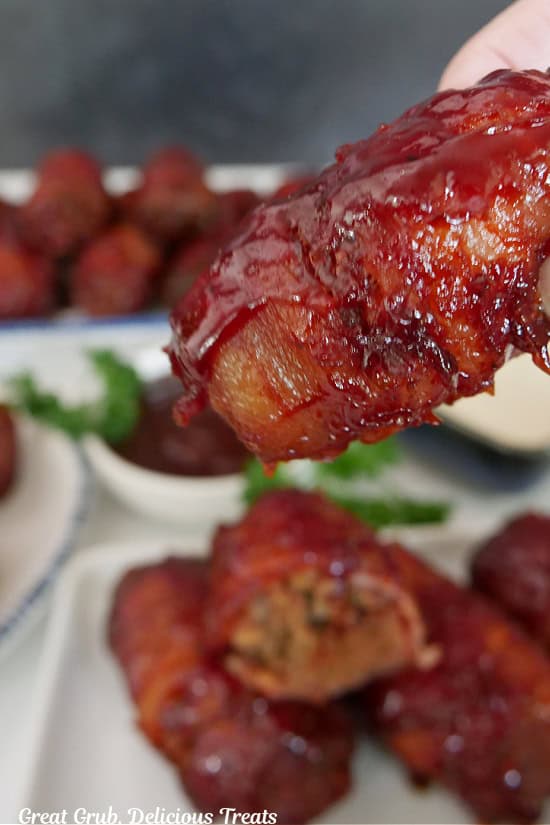 A smoked mini bacon wrapped meatloaf held above a plate of more mini meatloaves.