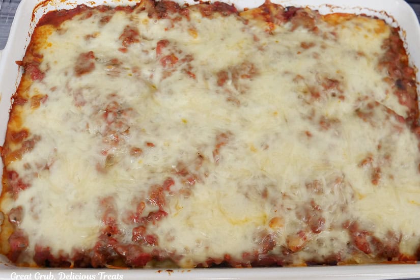 A white deep dish oblong baker filled with baked penne pasta right after being removed from the oven.