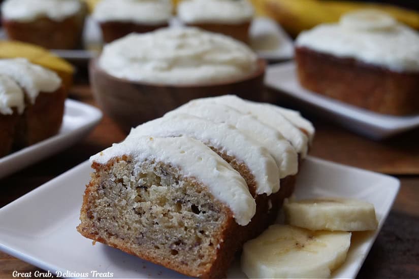 White plates with mini loaves of banana nut bread placed on a wood surface with a wooden bowl filled with frosting.