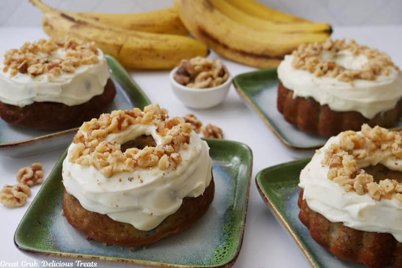 A white surface with four green and white plates with individual banana nut bundt cakes on them.