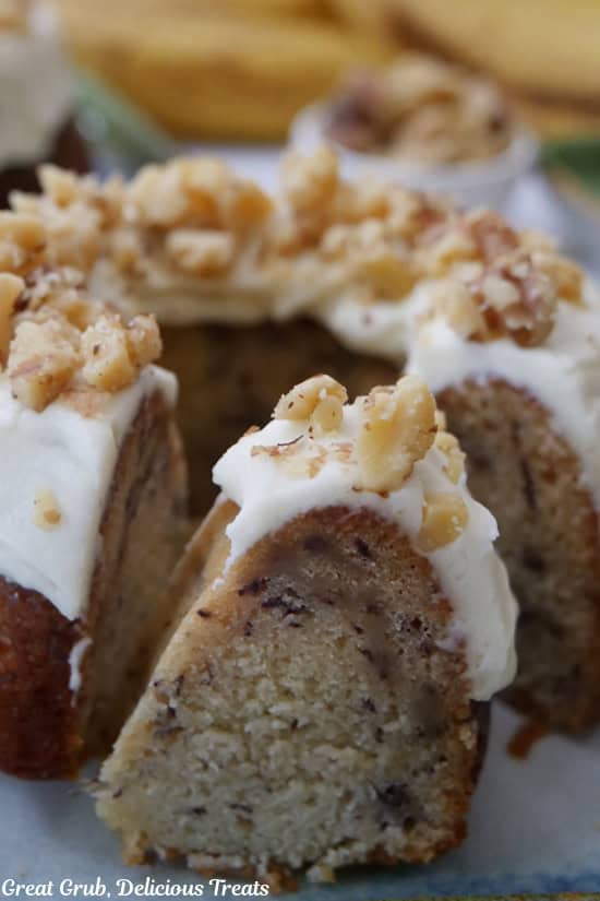 A bite of a banana bundt cake sitting on a plate with the individual cake right behind it.