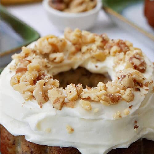 An individual banana bundt cake topped with cream cheese frosting and chopped walnuts.