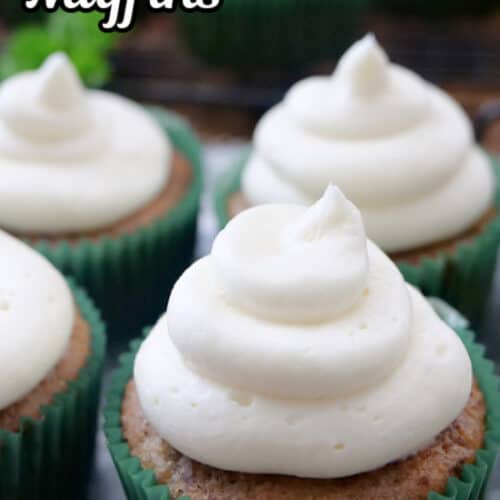 Four banana muffins on a silver plate that have cream cheese frosting on top.