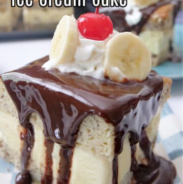 A slice of banana cake with hot fudge on top, a dollop of whipped cream, two slices of bananas, and a maraschino cherry.