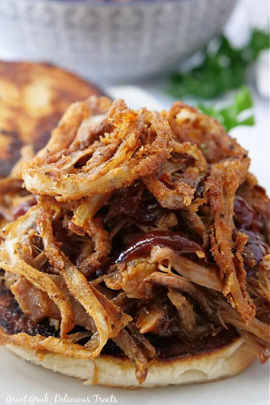 A close up photo of the bottom toasted bun loaded with barbecue pulled pork, crispy onion strings and BBQ sauce.