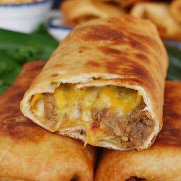 Three fried burritos on a white plate with blue trim with the top burrito cut so show the inside ingredients.