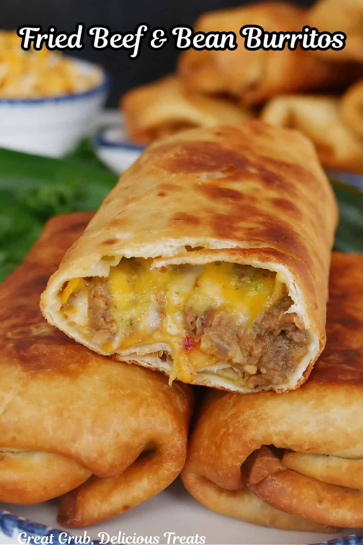 Three fried burritos on a white plate with blue trim with the top burrito cut so show the inside ingredients.