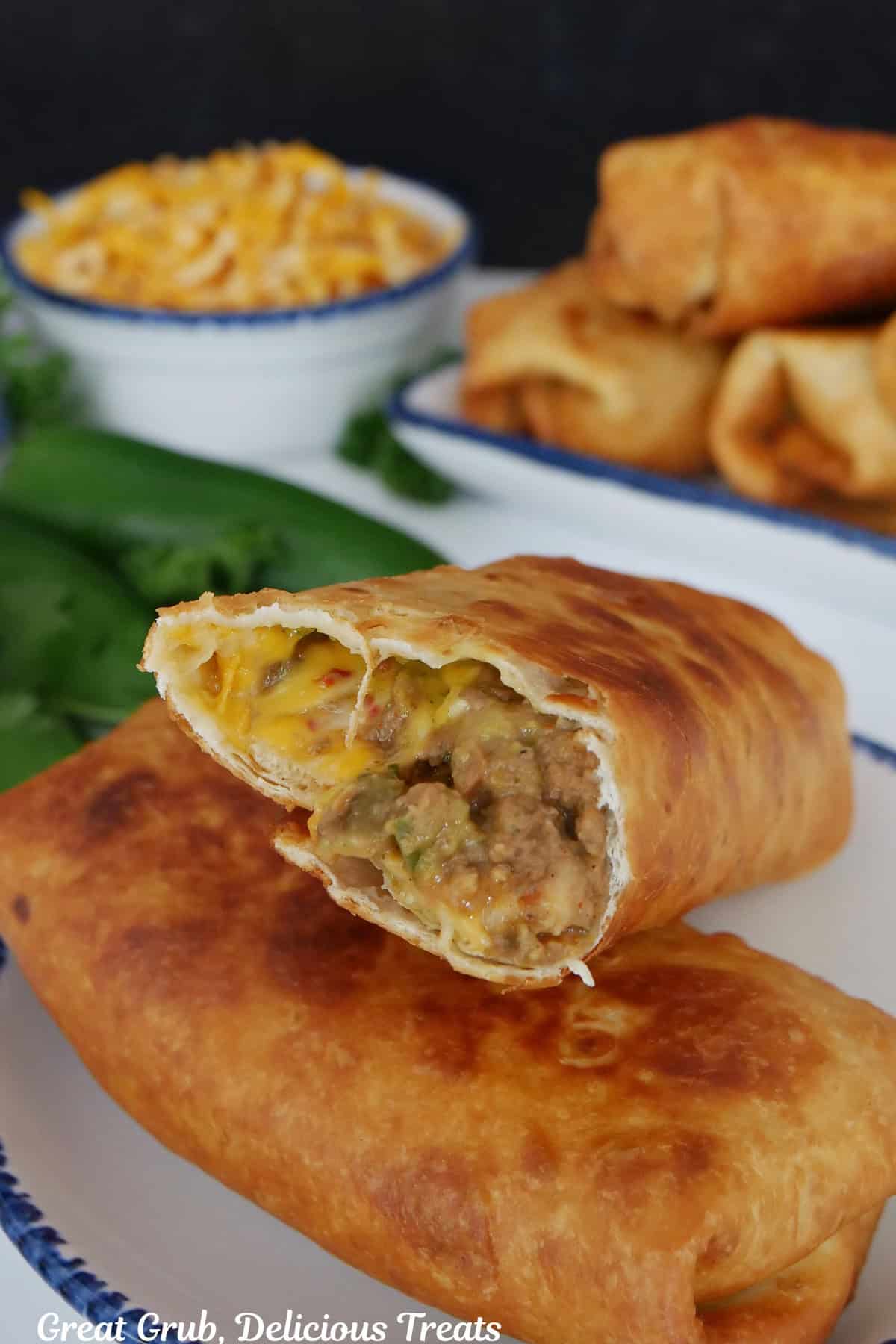 Two fried burritos on a white plate with blue trim with the top burrito open to show the inside ingredients.