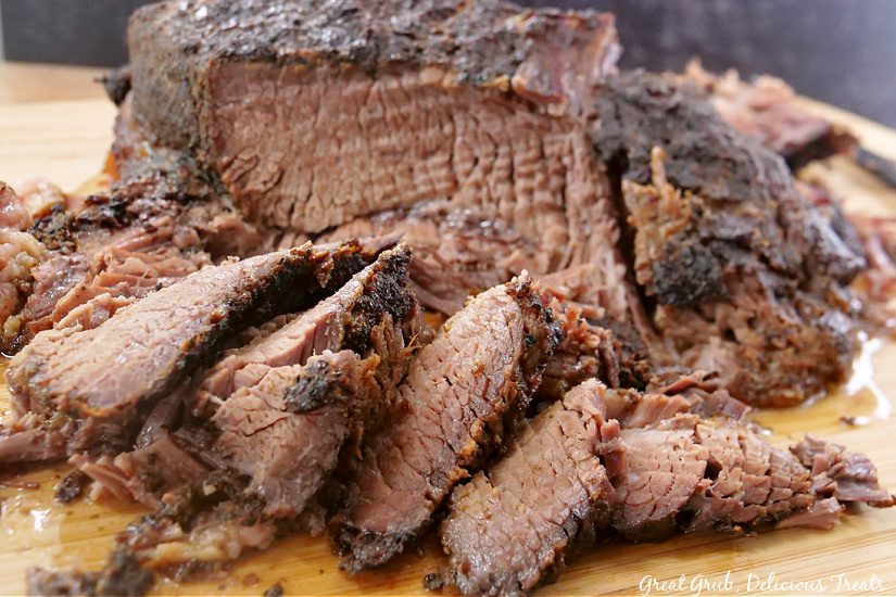 A brisket on a wood cutting board with slices of brisket laying in front of the brisket.