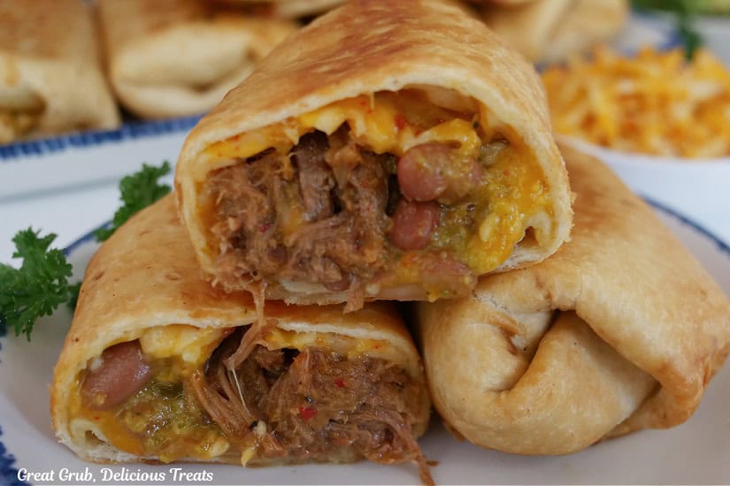 A white plate with two fried beef burritos on it with one of them cut in half.