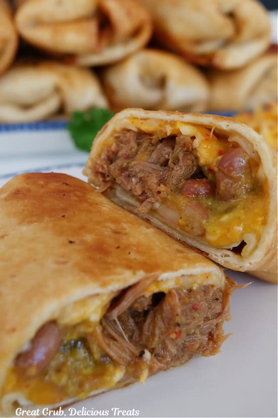 A fried beef burrito on a white plate that has been cut in half with more burritos in the background.