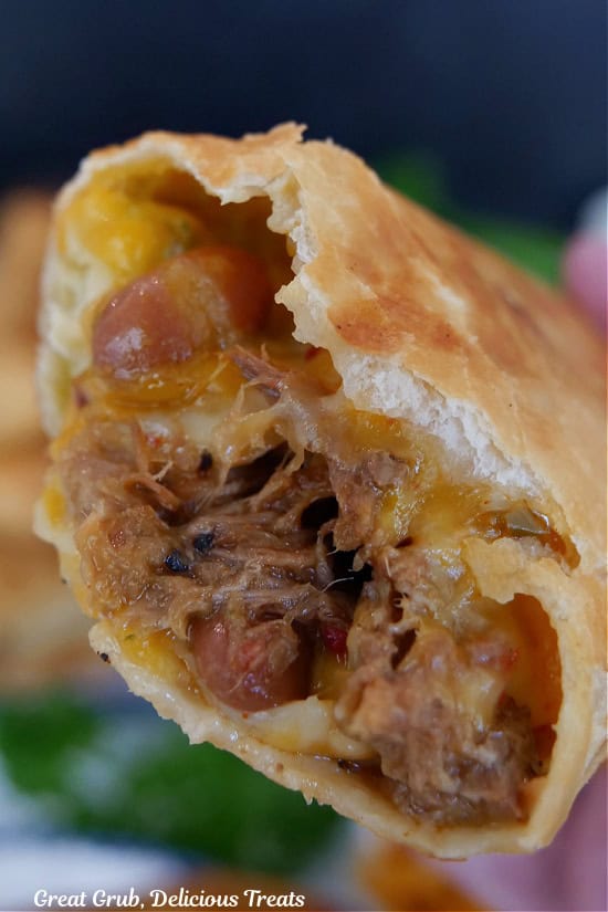 A fried beef burrito that is held up and has a few bites taken out of it.