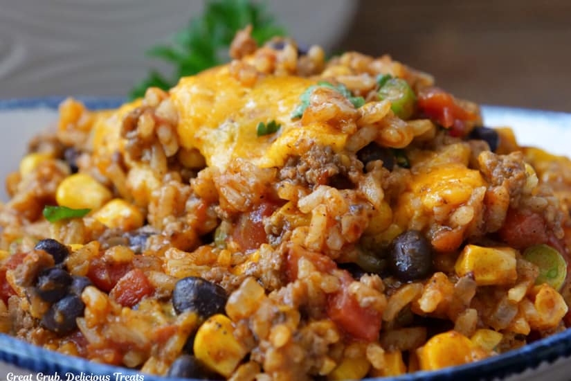 A horizontal photo of ground beef, rice, corn, beans, and cheese in a white bowl with blue trim.