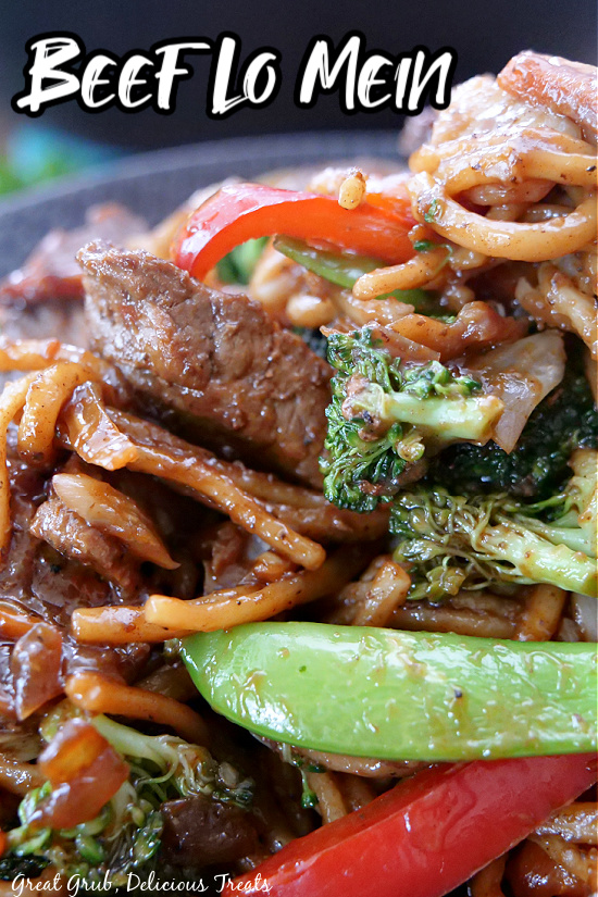 A close up pic of a bowl of beef lo mein with fresh veggies, noodles, beef, and coated in a sauce.