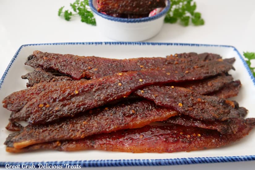 A horizontal photo of a white plate with blue trim filled with sliced candy bacon on it.