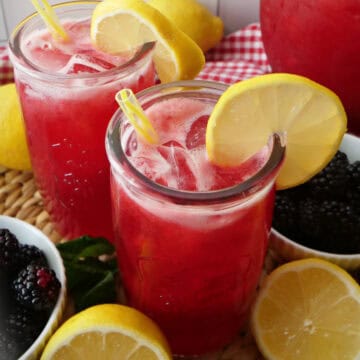 Two glasses and a picture of blackberry lemonade with fresh blueberries and lemon placed around them.