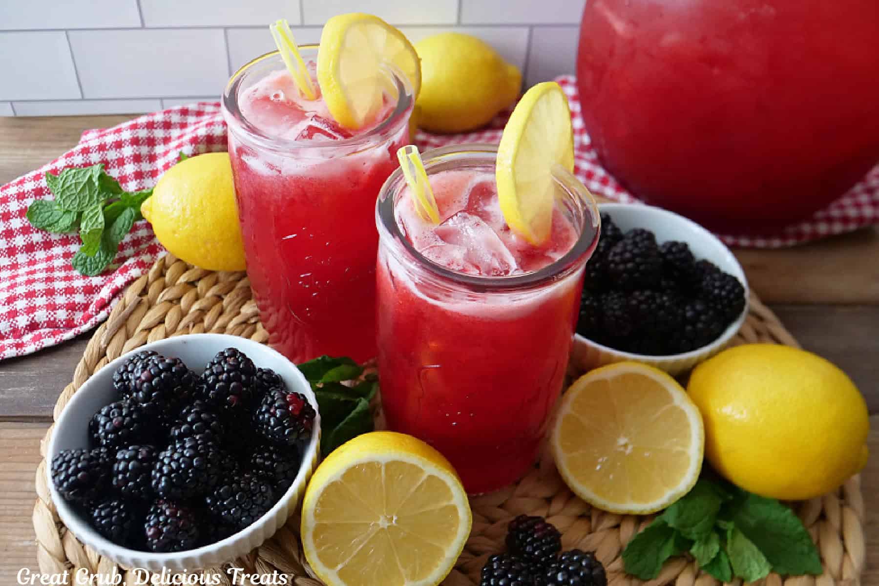 Two glasses filled with blackberry lemonade with fresh blackberries and lemons placed around the glasses.