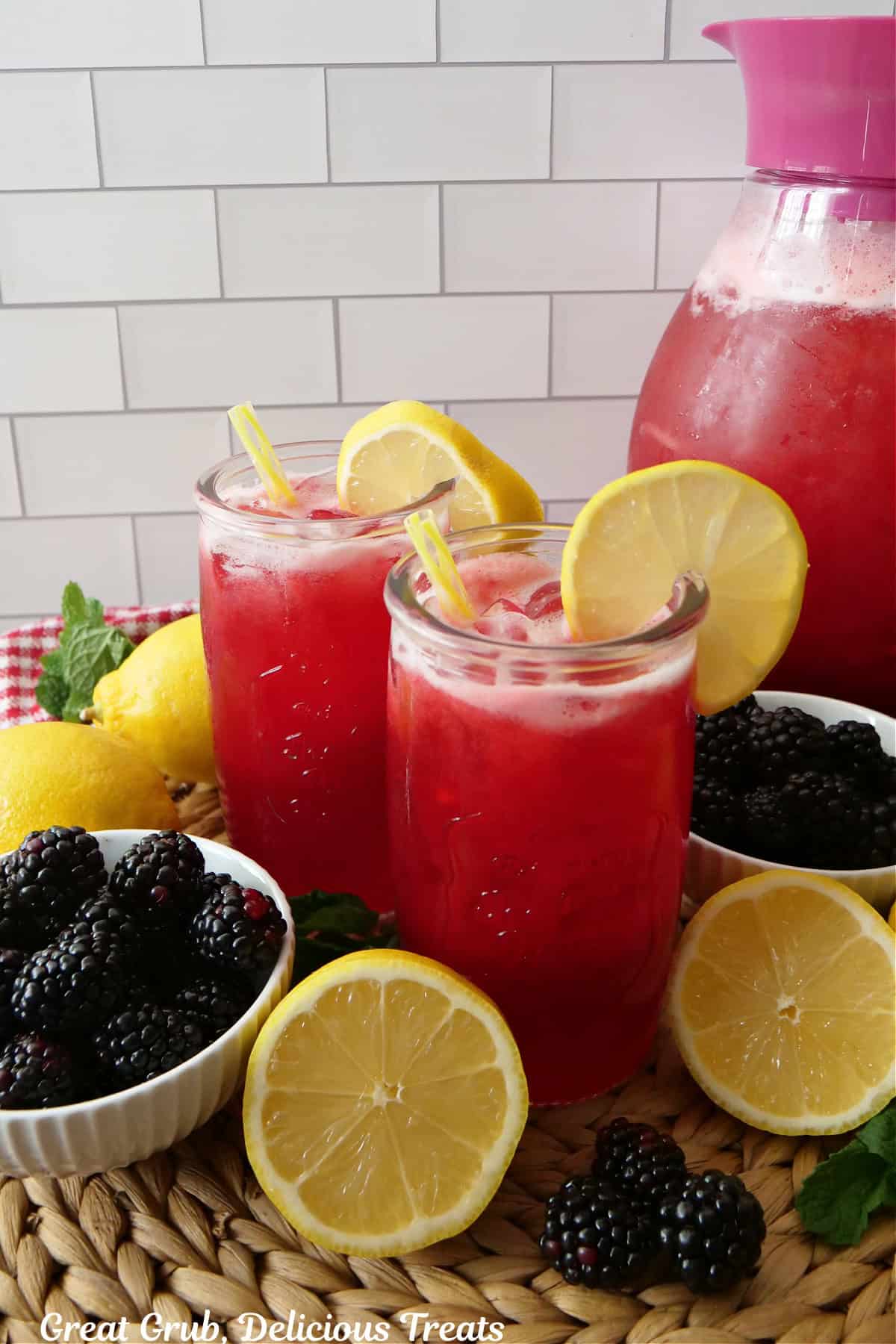 Homemade blackberry lemonade in two glasses with a pitcher filled in the background.