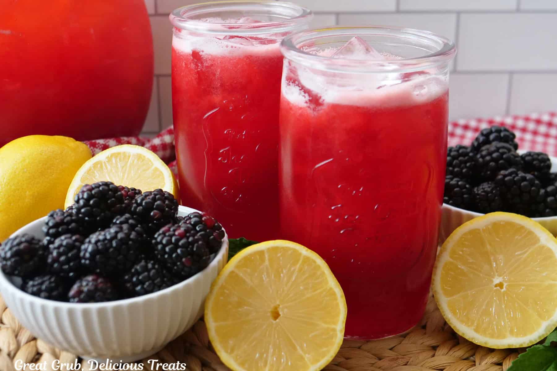 Two glasses filled with homemade blackberry lemonade with fresh lemons and blackberries around the cups.