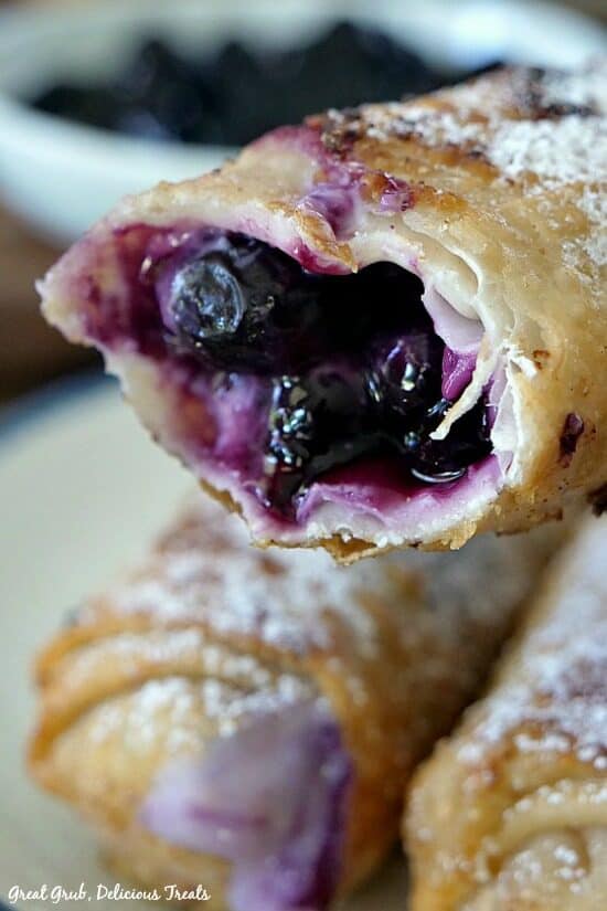 Blueberry Cream Cheese Egg Rolls are crispy and delicious, filled with fresh blueberries and a cream cheese filling. A close up photo of a blueberry egg roll with a bite taken out showing the inside filling.