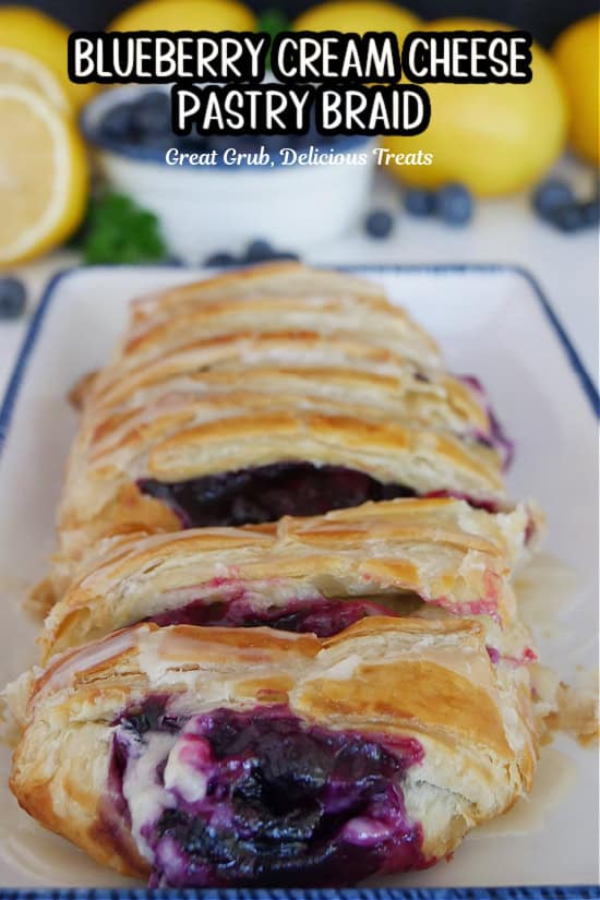 A white rectangle plate with blue trim with a baked and sliced blueberry pastry braid on it.