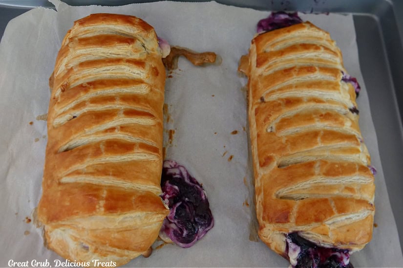 A baking sheet with two baked blueberry cream cheese pastry braids on it.