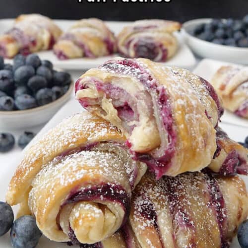 White plates with blueberry pastries on them with a white bowl filled with blueberries.