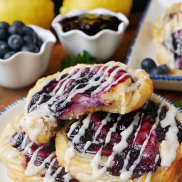 A round white plate with blue trim with three blueberry danishes on it with a bite taken out of the one on top.